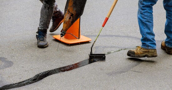 Road surface restoration work in the worker performs on road patcher work on the repair of cracks by filling and sealing with coated by bitumen emulsion
