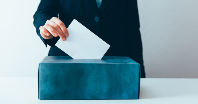 Close-up of voter putting ballot into voting box.
