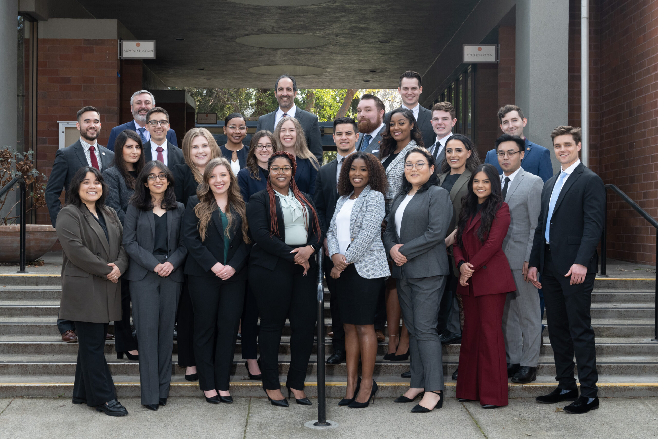 A group photo of 20 people wearing suits posing on stairs outdoors