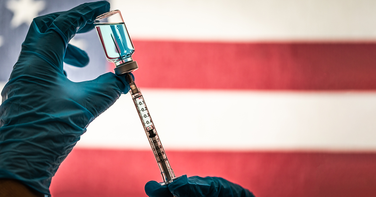 Front Line Worker Holding Syringe and Vial Filled with Coronavirus Vaccine or Medicine Silhouetted Against American Flag