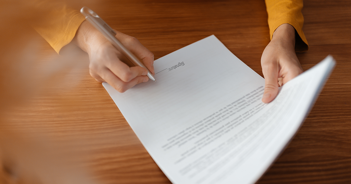 Close up image of an unrecognizable person's hands signing a business document on a wooden desk. Business concept.