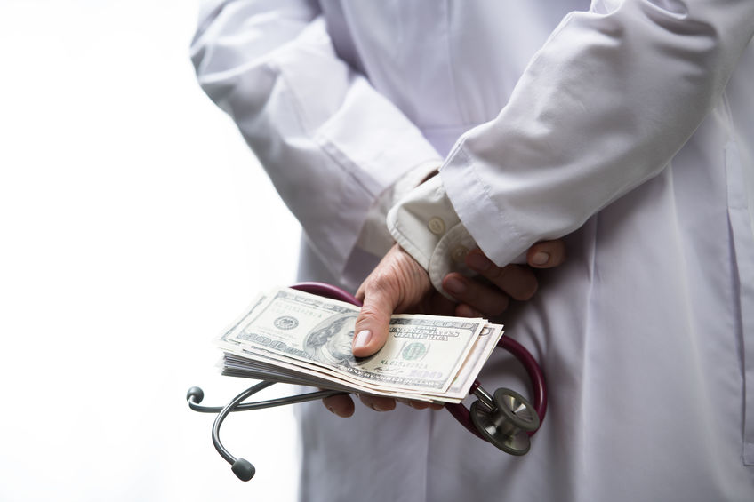 Medical doctor holding money and stethoscope in hospital setting