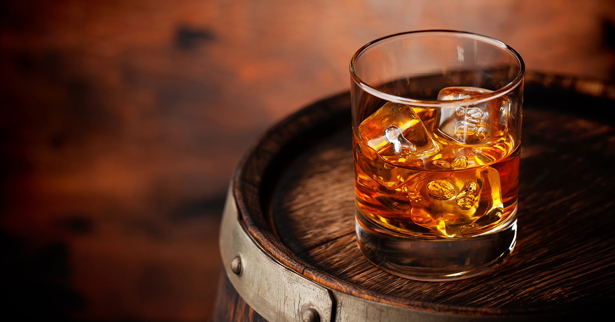 Glass of whiskey with ice cubes on the old barrel