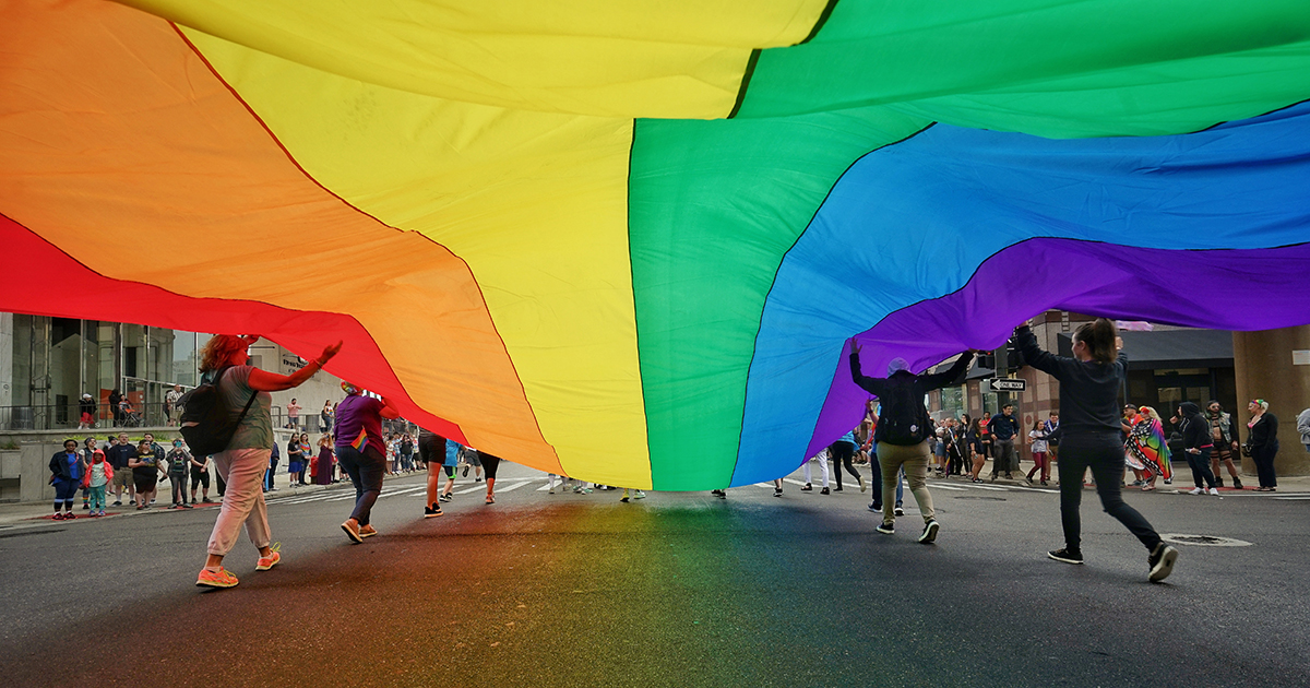 People Holding Large Colorful Flag While Walking On City Street