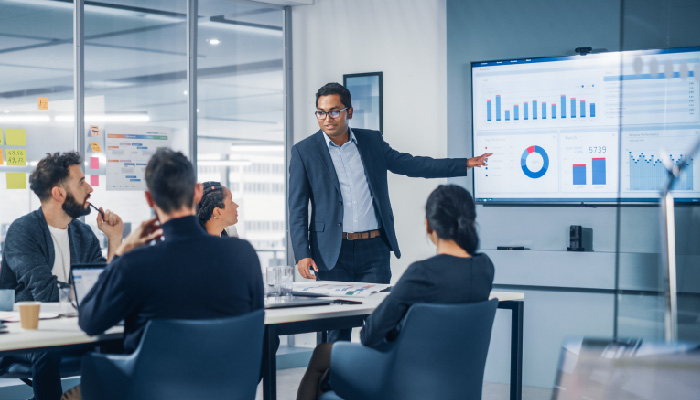 A male coworker stands and gives a presentation to his team