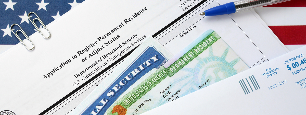 I-485 Application to register permanent residence or adjust status form and green card from dv-lottery with social security number lies on United States flag with USCIS envelope