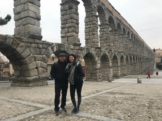 A person and person posing for a picture in front of a stone bridge Description automatically generated