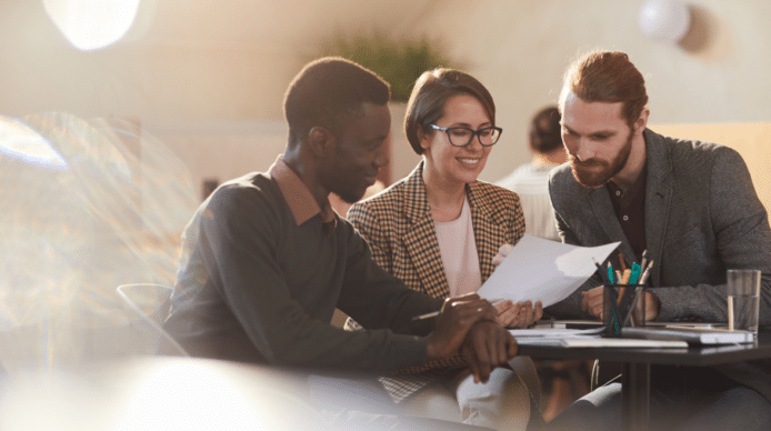 3 people sit around a table looking at a paper document