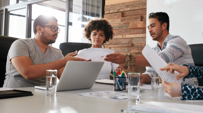Two men and a woman in casual clothes at a conference table examining a paper document