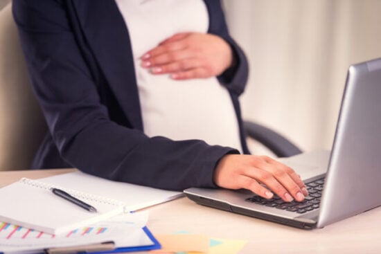 A,Pregnant,Woman,Hand,On,Belly,Closeup,Uses,Laptop,In