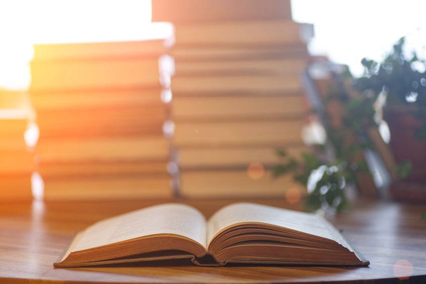 Book background. Blurred open book on a table in a university or school library in the sunlight from the window. Reading, literature, study and knowledge concept.