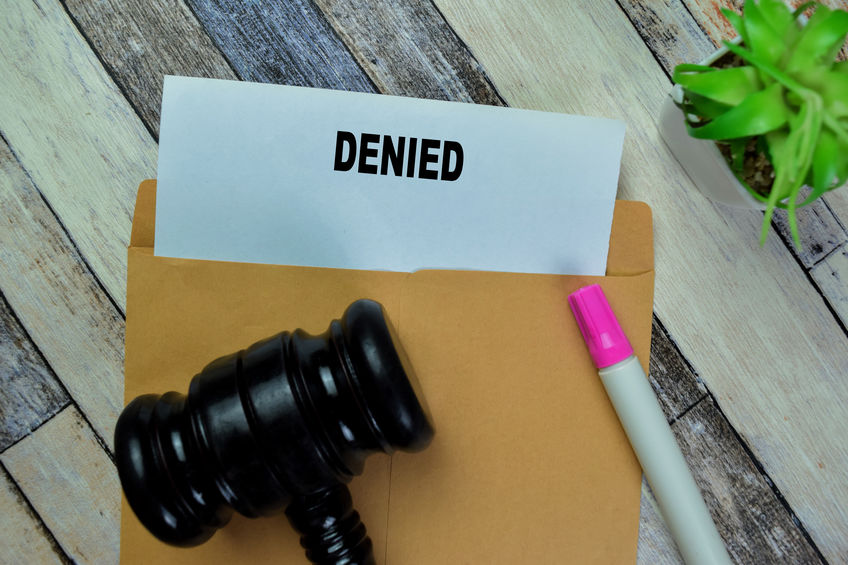 Concept of Gavel and Denied text above brown envelope isolated on on Wooden Table.