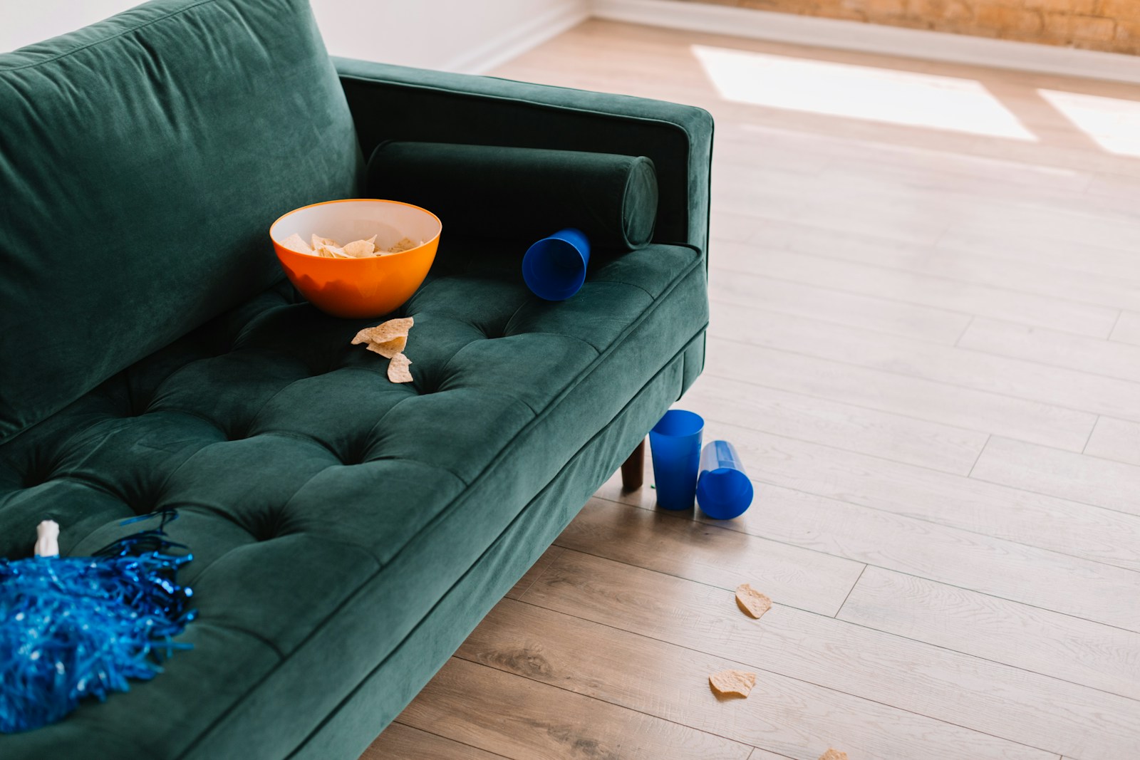 Green couch with a bowl of chips spilled with blue cups and blue pom poms