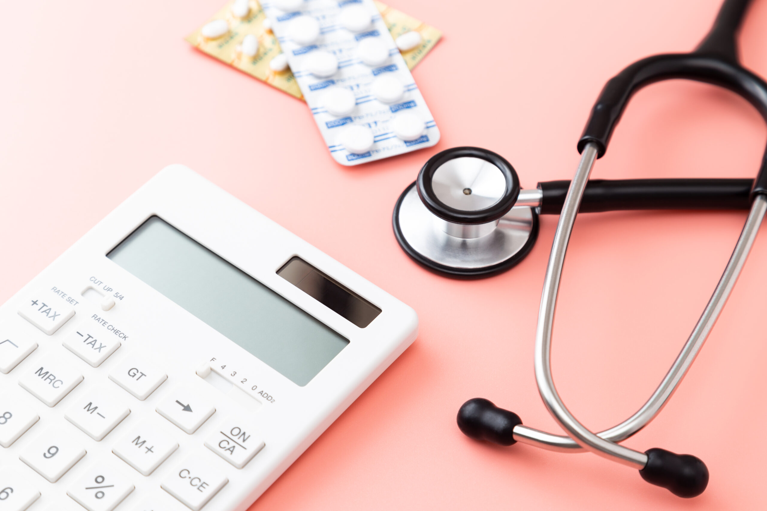 GettyImages-1681769150 Stethoscope, calculator and pills on pink background.