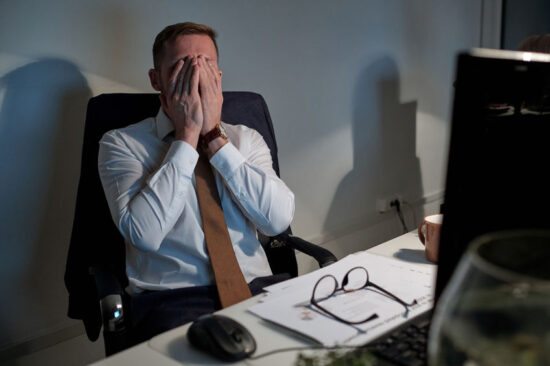 Exhausted businessman covering his face by hands by workplace