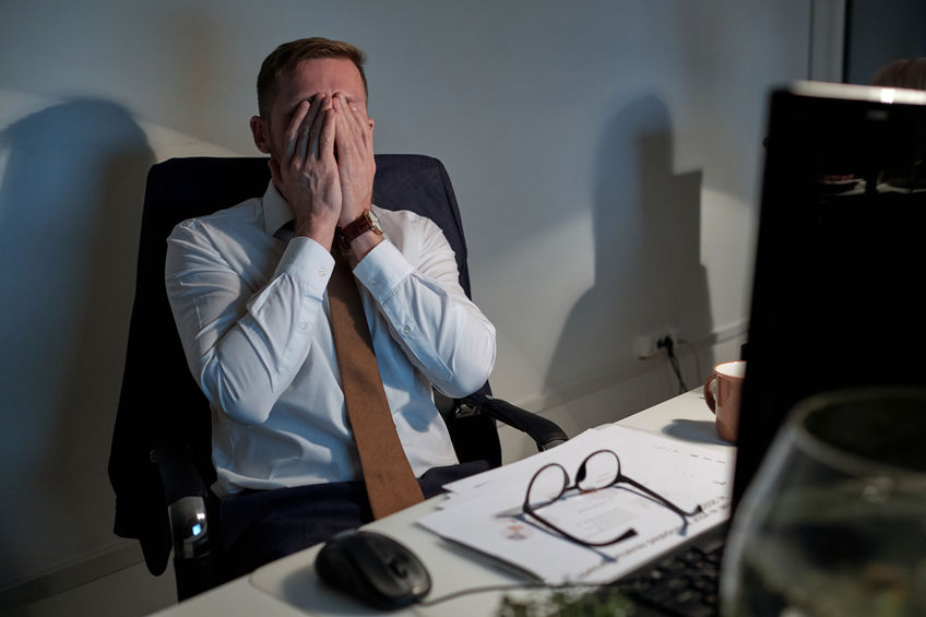 Exhausted businessman covering his face by hands by workplace