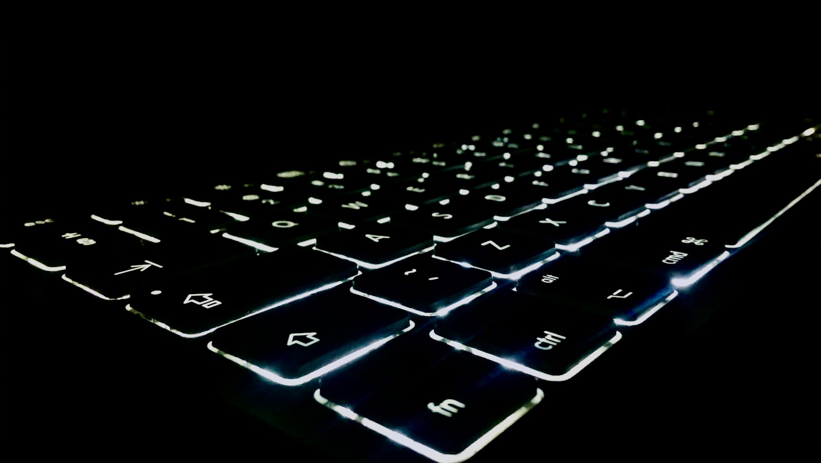 A close-up of an illuminated keyboard in a dark setting, highlighting the glowing keys with sharp focus. The image captures the modern and sleek design, perfect for technology-related themes or backgrounds.
