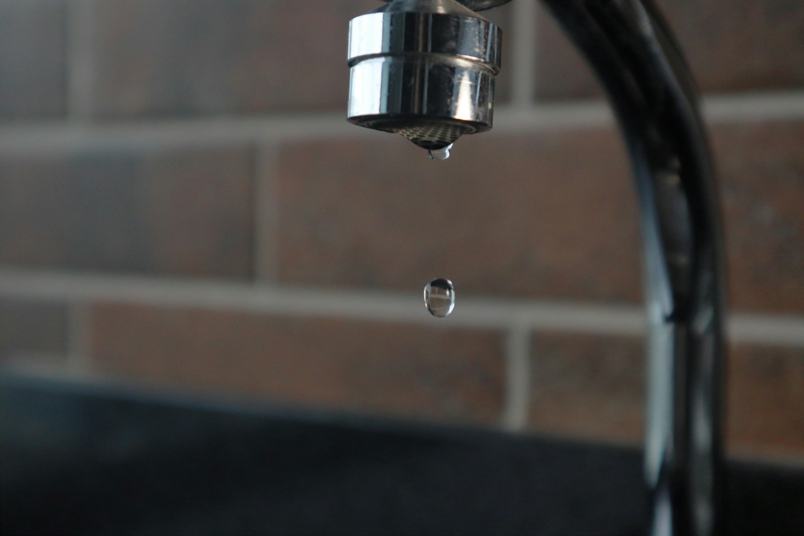 faucet drops water on brick background