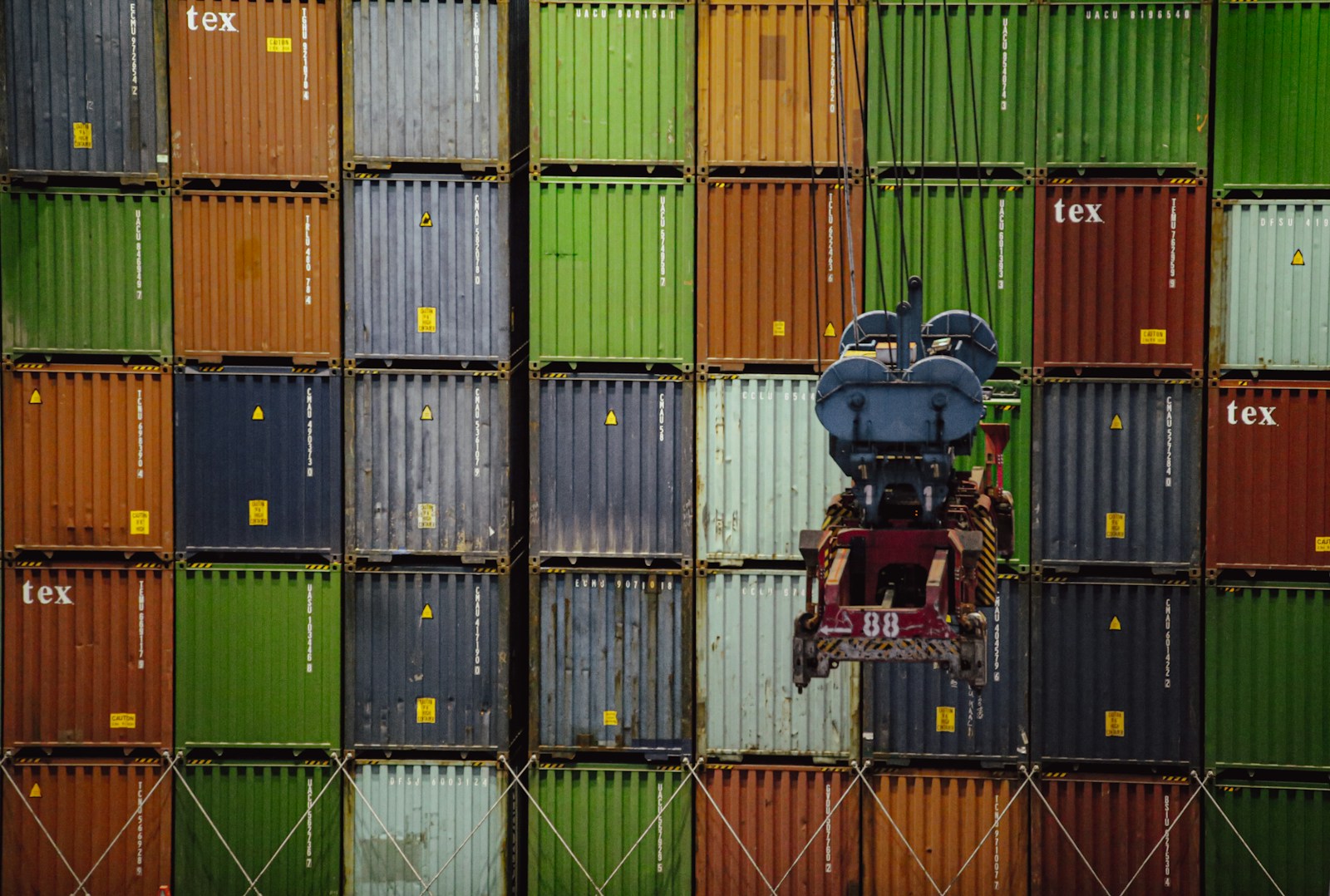 Close-up of multicolored stacked shipping containers with a container spreader from a crane positioned in front, ready for loading or unloading operations.