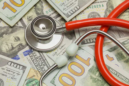 Red stethoscope with a pile of hundred dollar bills.