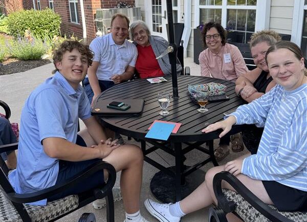 A family looking at the camera smiling while gathered around a table outside on a summer day