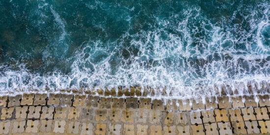 Emerald waves washing off the seawall constructed of small cubical concrete structures