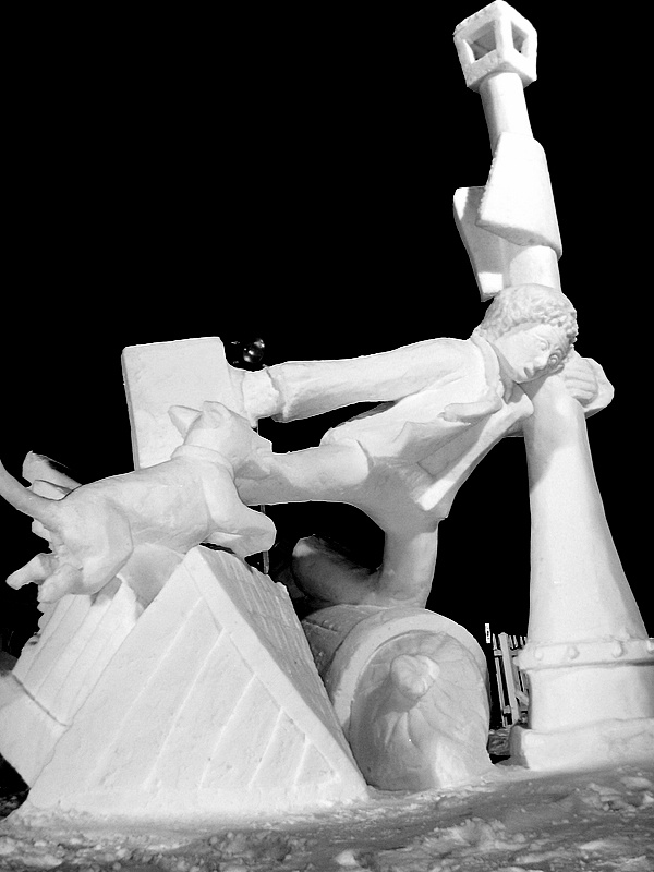 Finished snow sculpture of boy and dog hanging on to a light post against the wind.