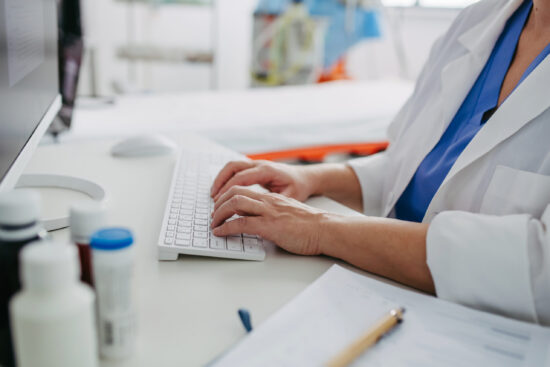 Close up of doctor working on computer in doctor's office. Physician doing paperwork and administration.