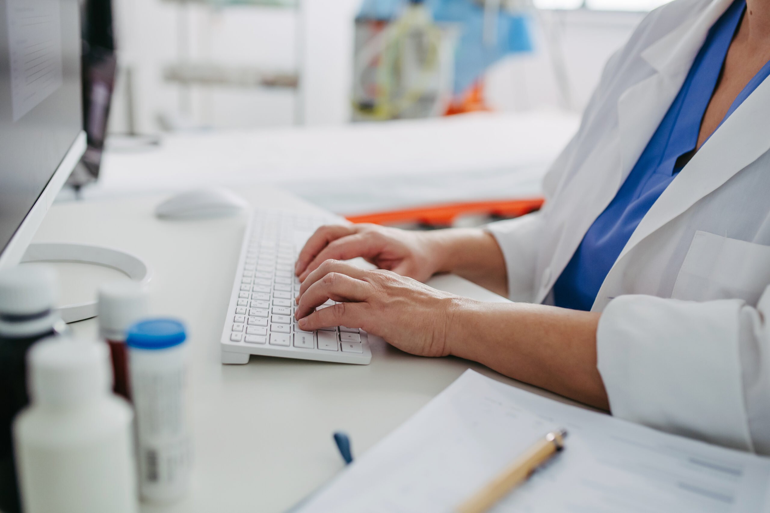 Close up of doctor working on computer in doctor's office. Physician doing paperwork and administration.