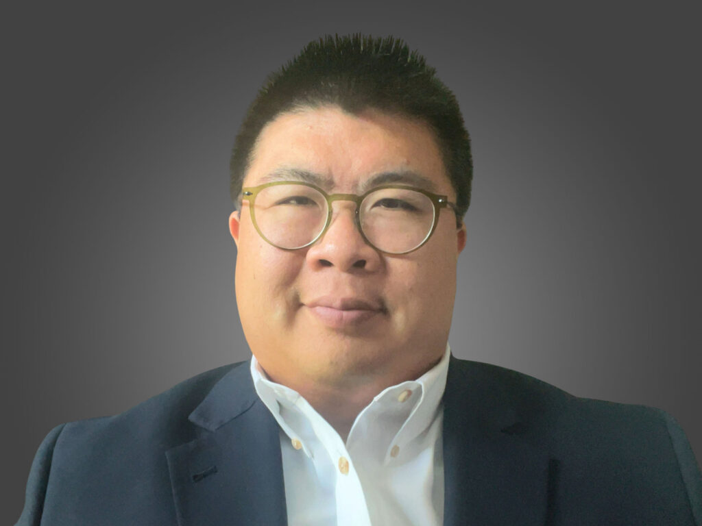 Portrait of a man wearing glasses and a dark blazer against a gray background