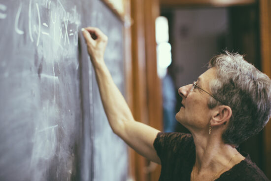 Mathemathics professor at chalkboard writing formula