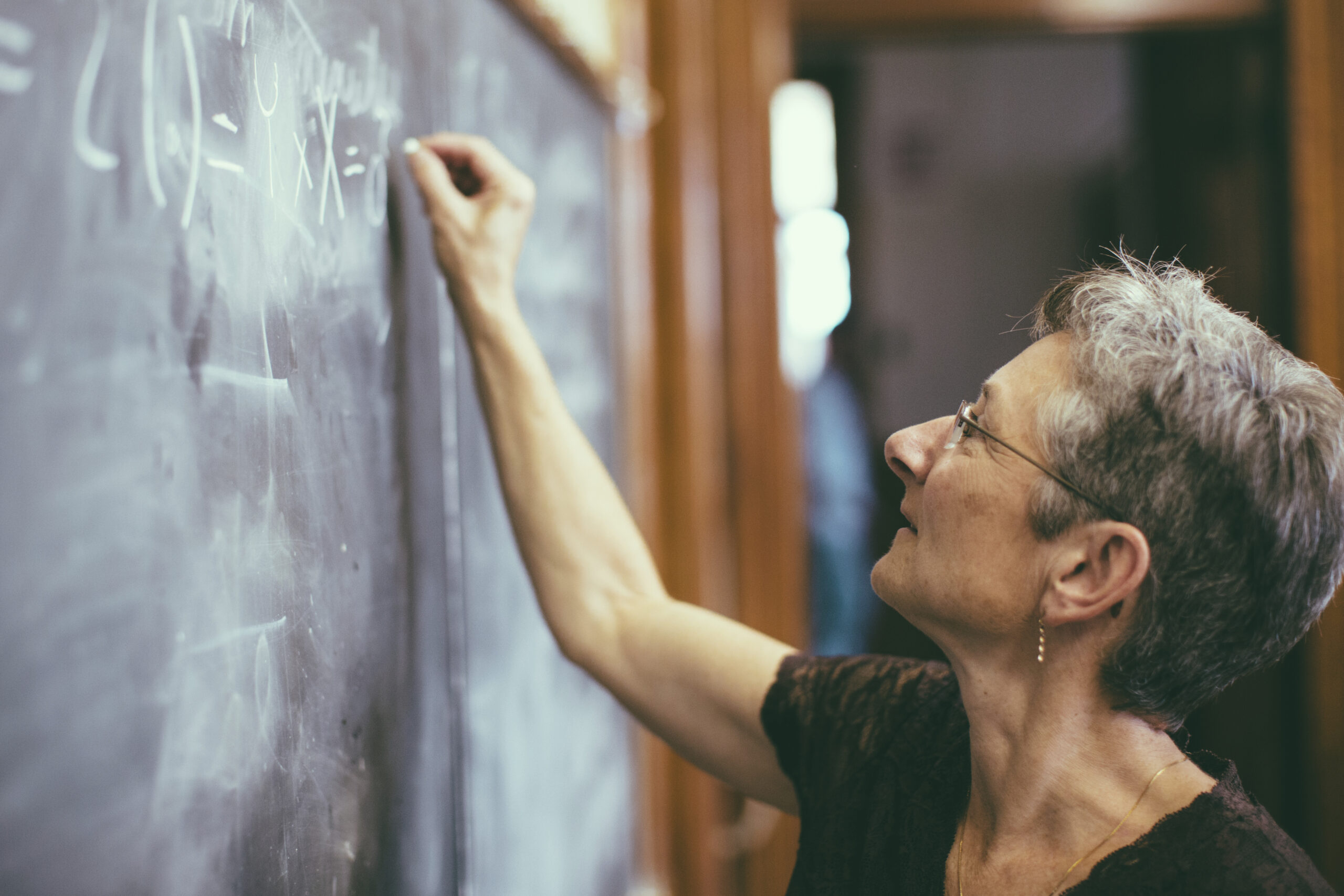 Mathemathics professor at chalkboard writing formula