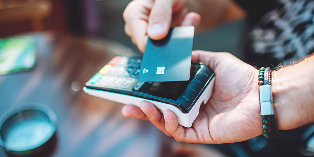 Adult man paying with credit card at cafe, close-up of hands with credit card and credit card reader