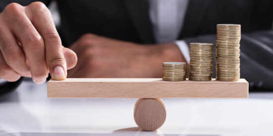 Businessperson Balancing Stacked Coins On Wooden Seesaw