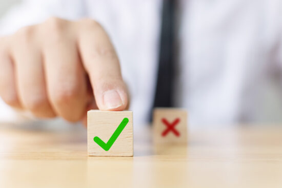 Hand of a businessman chooses checkmark and x sign symbol on wooden cube block