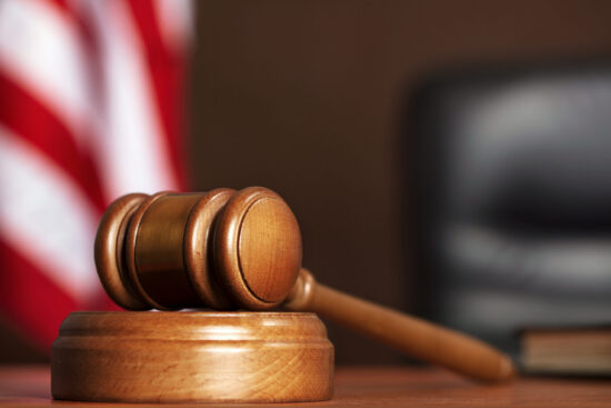 Wooden gavel on the table of judge with american flag and black chair