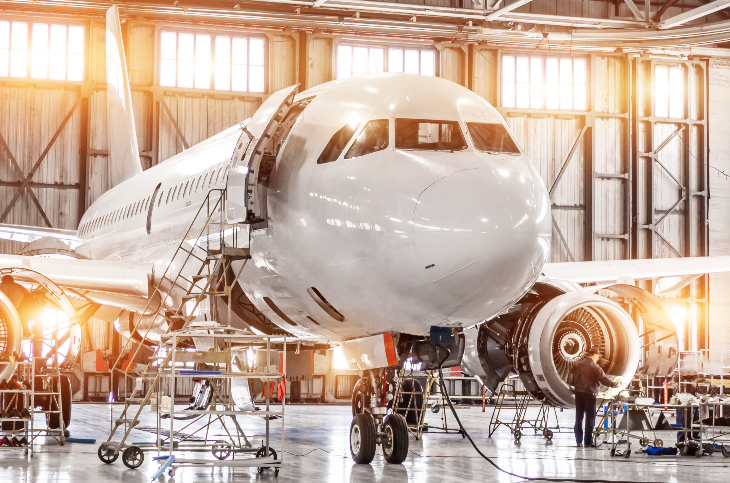 Passenger commercial airplane on maintenance of engine turbo jet and fuselage repair in airport hangar. Aircraft with open hood on the nose and engines, as well as the luggage compartment.