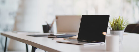 Open blank laptop in modern workplace with office supplies and decorations on white table