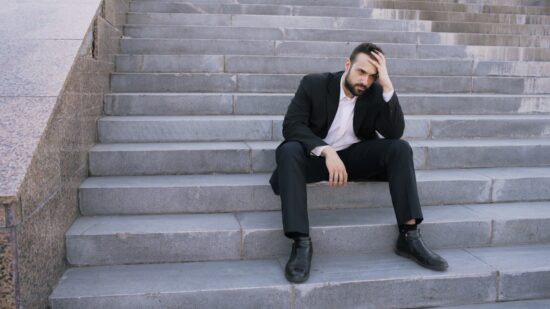 Upset young business man having stress and sitting on stairs in street. Businessman having deal problems at work concept