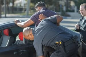 How to Refuse a Police Search of Your Car (and Take Back Consent) 3 Police officer conducting a pat-down of a man beside a car while another officer observes.