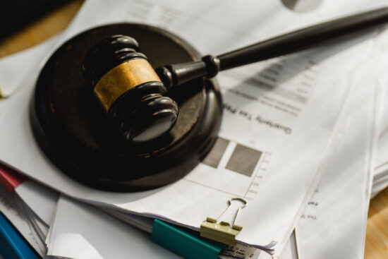 Wooden gavel rests on documents. Paperwork piles beneath a judge's hammer. Clips and pens lie nearby, ready for use. Legal matters feel urgent and serious. Ideal for law, finance, or courtroom themes