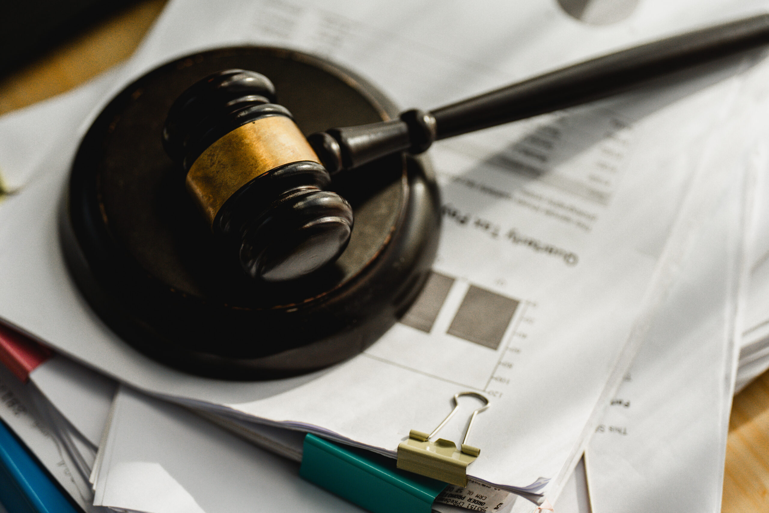 Wooden gavel rests on documents. Paperwork piles beneath a judge's hammer. Clips and pens lie nearby, ready for use. Legal matters feel urgent and serious. Ideal for law, finance, or courtroom themes
