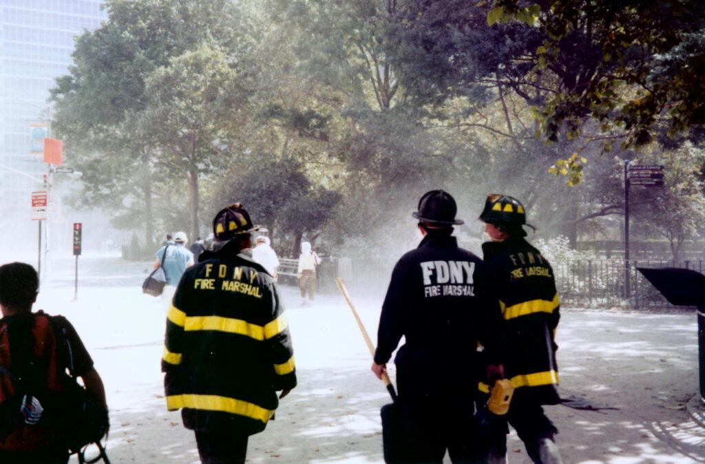 FDNY fire marshals walking through a dust-covered Battery Park near the Statue of Liberty ferry signs