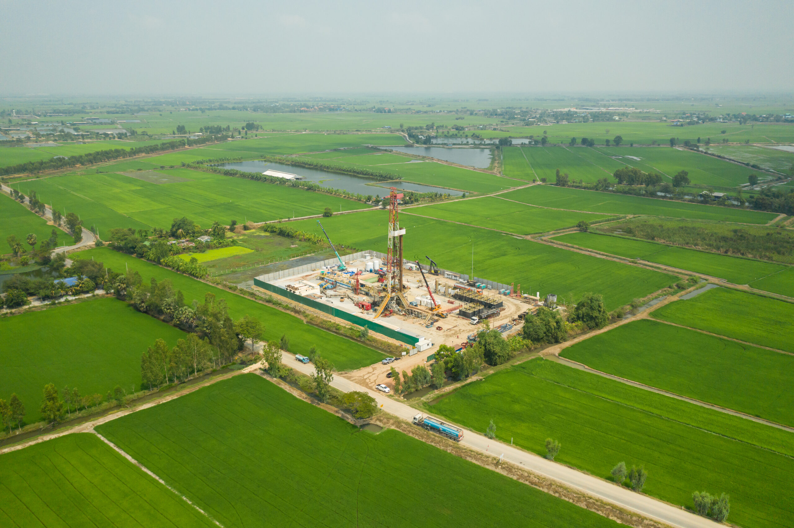 Oil and gas land drilling rig onshore in the middle of a rice field aerial view from a drone