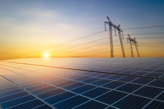 High voltage pylons with electric power lines transfering electricity from solar photovoltaic sells at sunrise. Production of sustainable energy concept