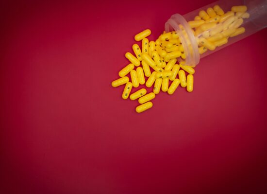 Yellow pills overflowing from bottle on red background